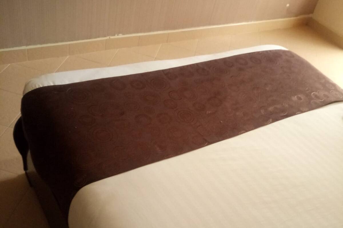 A bed with a patterned brown headboard and a plain white mattress.
