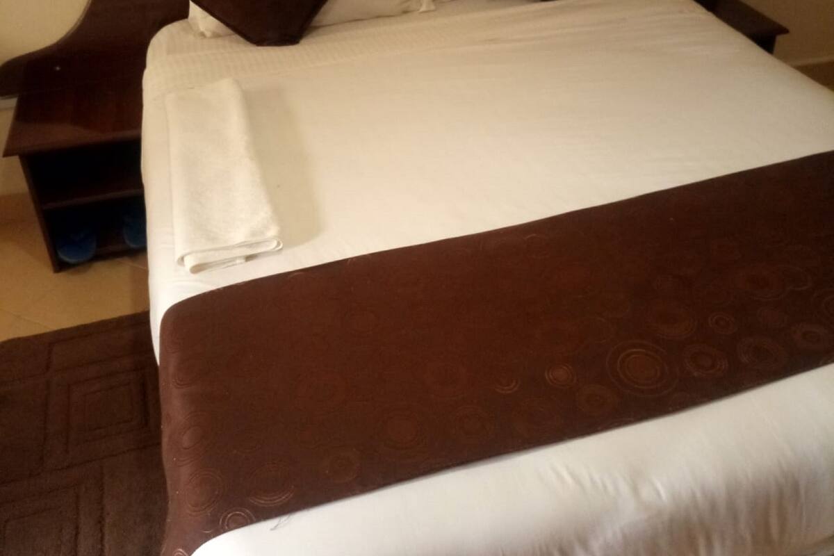 A neatly made bed with a brown headboard, white bedding, and a white towel on the side.