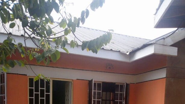 A small, enclosed outdoor area with a concrete floor, a door leading inside, and a window with bars. - Peacock Restaurant (Nyeri)