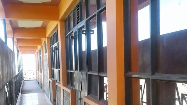 A long corridor with tiled flooring, large windows with metal grilles, and a ceiling fan. - Puya Lodge (Kitengela)