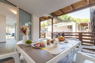 Uma mesa de jantar com itens de café da manhã, um vaso com flores secas e vista para uma área residencial.