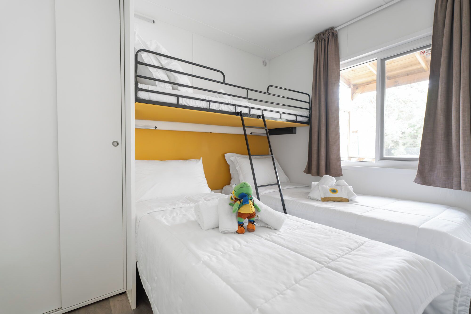 A bunk bed room with a ladder, white bedding, and a window with curtains.