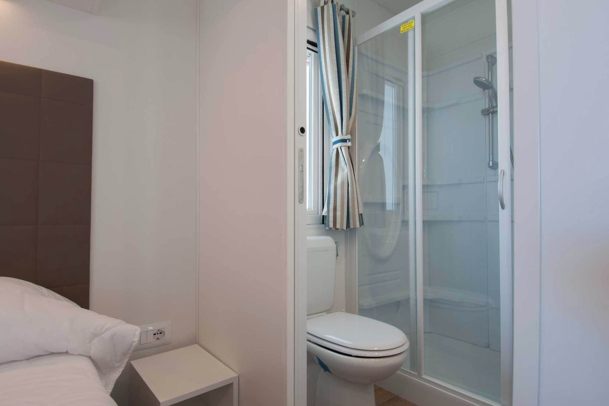 Ein Badezimmer mit Toilette, Duschkabine und Nachttisch mit Kissen.