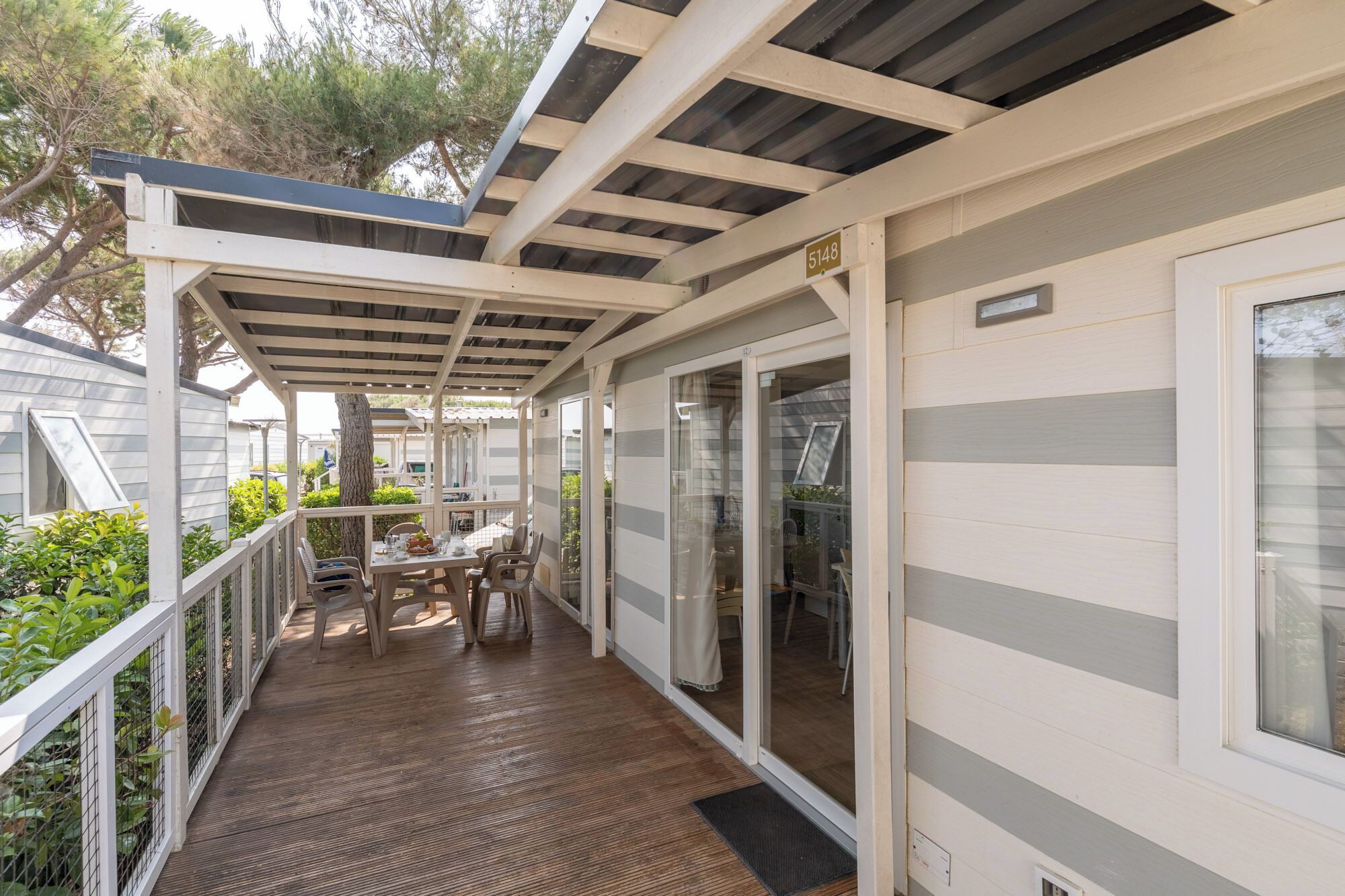 Un espace extérieur abrité avec une table et des chaises, une terrasse en bois et un bâtiment portant un numéro.