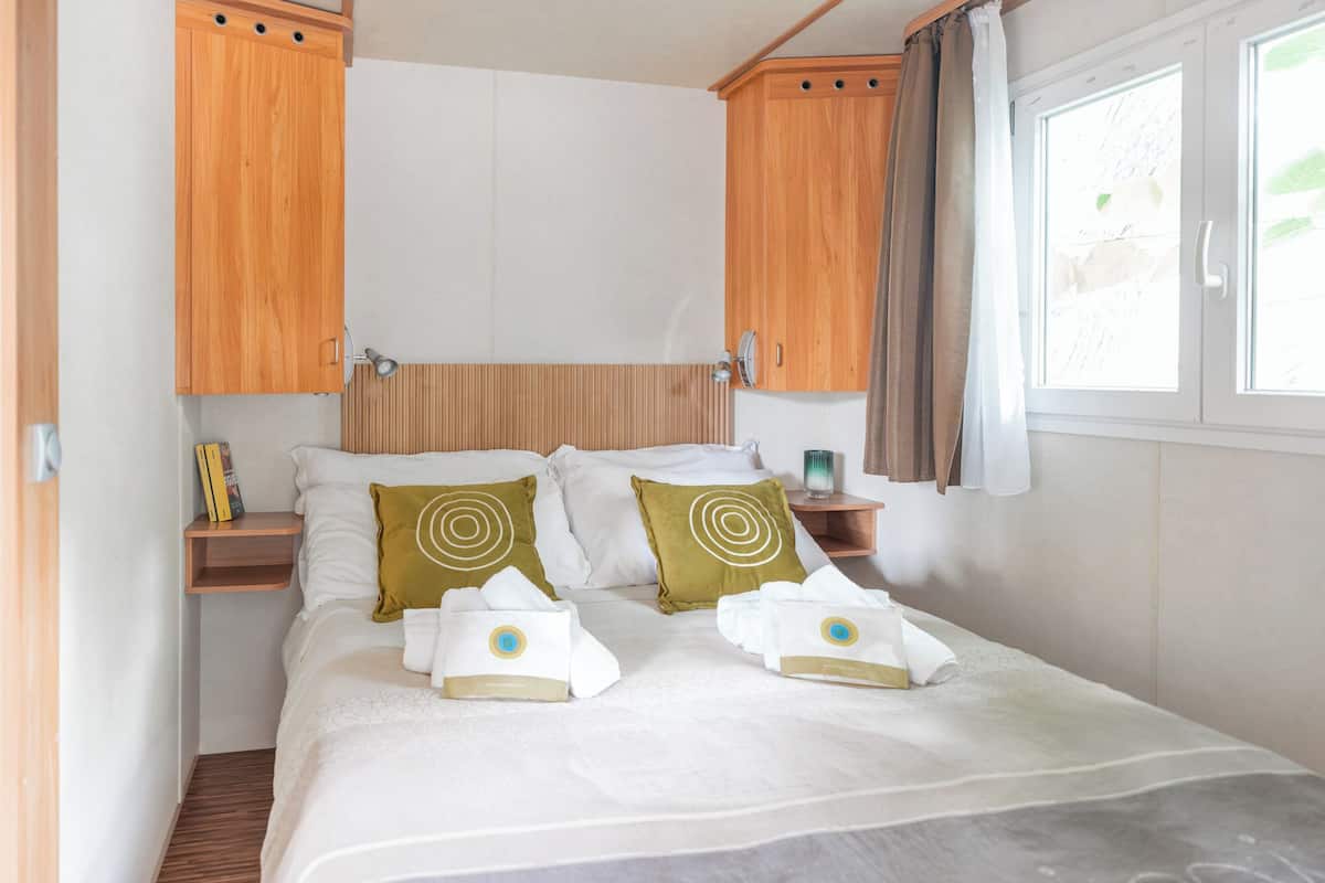Une chambre à coucher avec un lit, deux oreillers, une table de chevet avec une lampe et des armoires en bois au-dessus du lit.