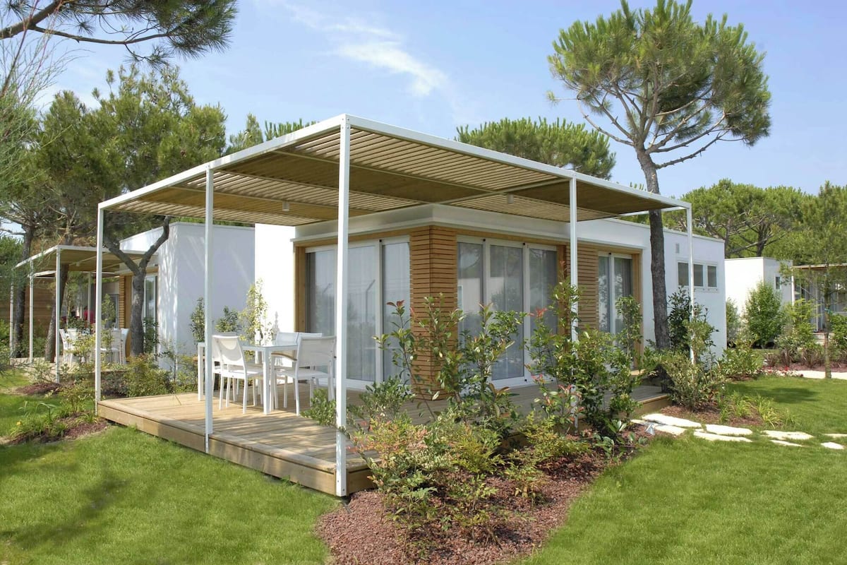 Une maison moderne de plain-pied, dotée d’un patio couvert, d’une petite terrasse et d’un jardin où poussent différentes espèces de plantes.