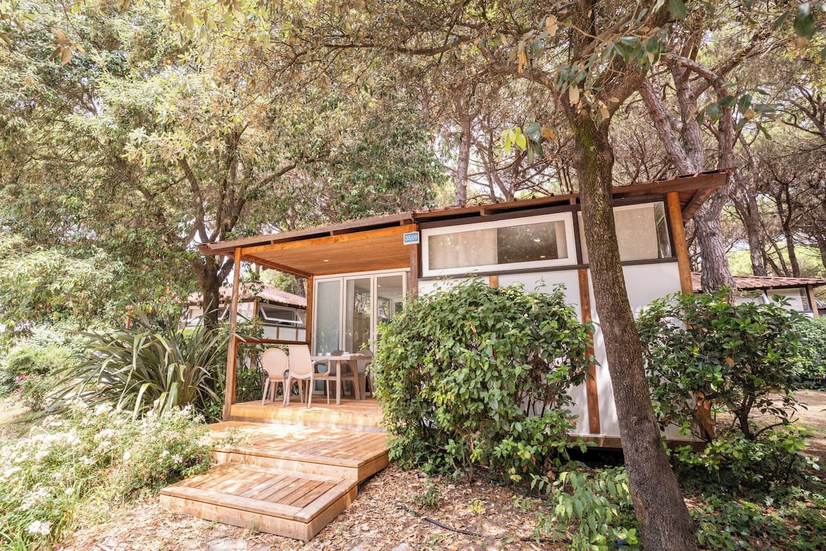 Une terrasse en bois avec une table et des chaises, entourée d’une végétation luxuriante et d’arbres.