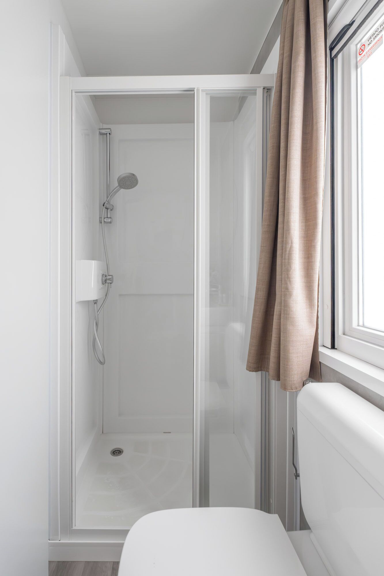 A modern bathroom with a glass-enclosed shower, a toilet, and a window with curtains.