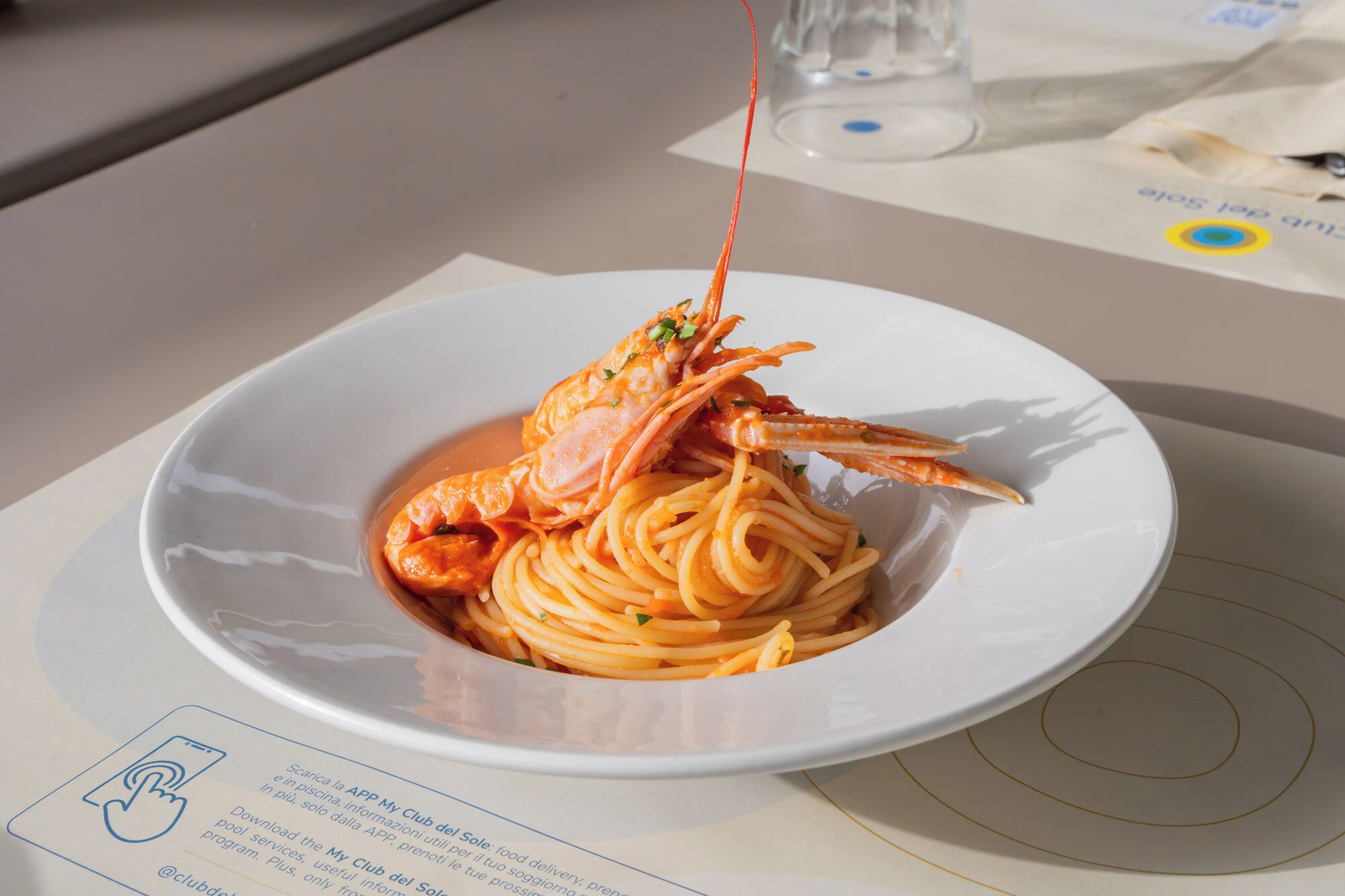 Lautasella on spagettia ja sen päällä hummerin pyrstä. Lautanen on asetettu pöydälle, jonka päällä on myös ruokalista.