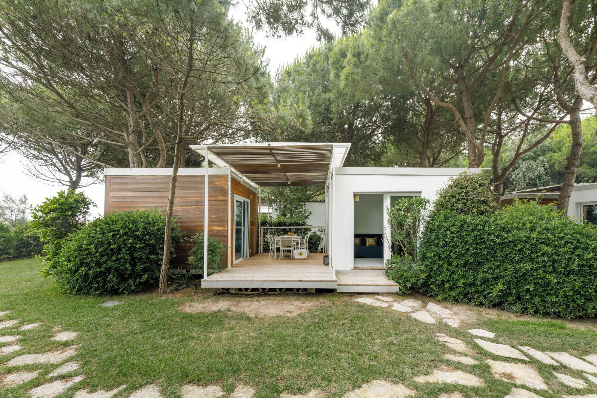 Ein modernes Haus mit einer Holzterrasse, einer überdachten Veranda und einem Garten.