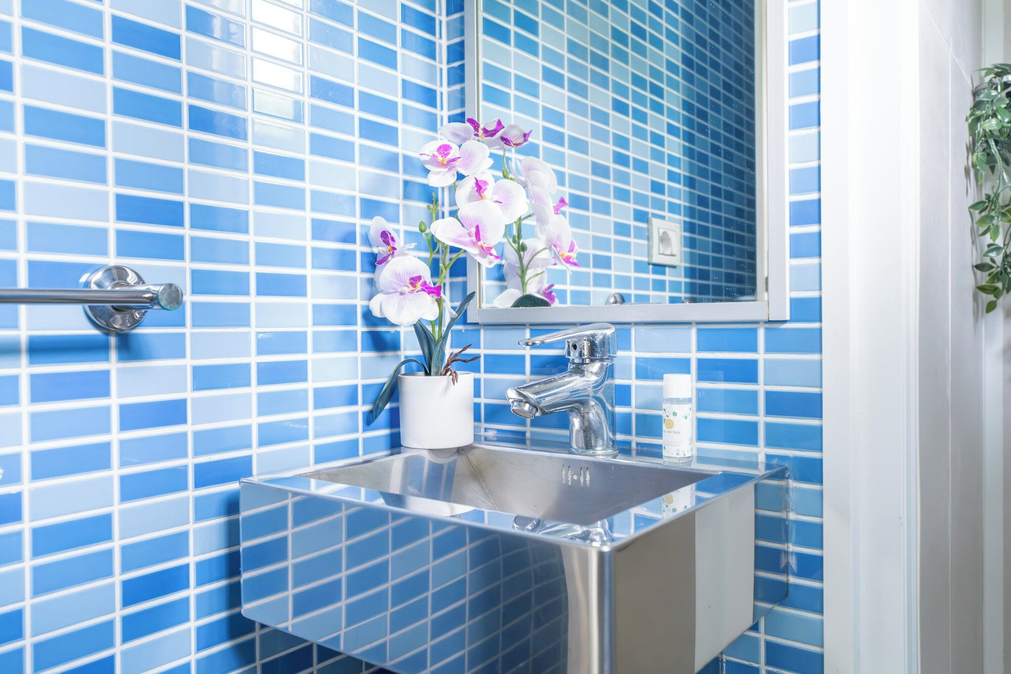 A bathroom with blue tiled walls, a sink, a mirror, and a potted orchid.