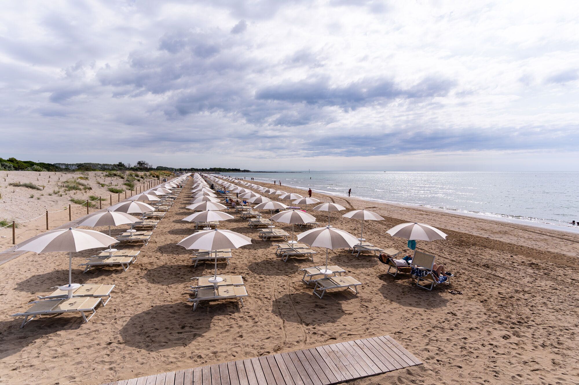 A beach with rows of sun loungers and umbrellas, a wooden boardwalk, and the ocean in the background.