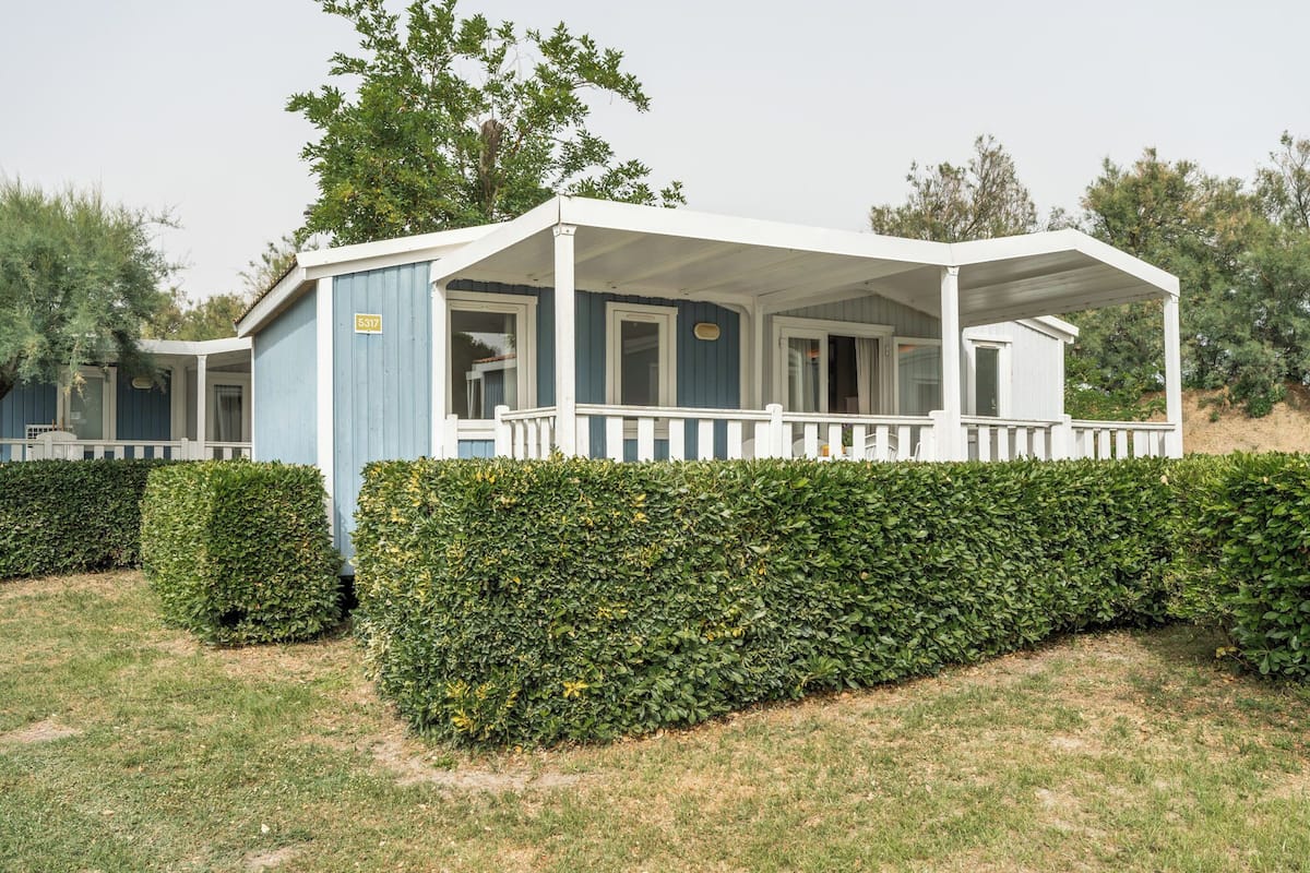 A single-story house with a porch, a number sign, and a well-maintained hedge.