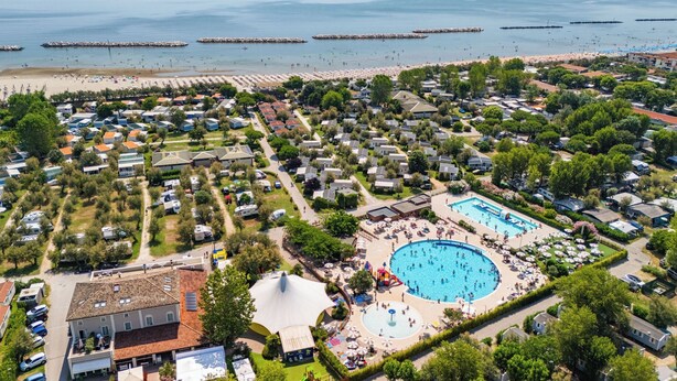 An aerial view of a vacation area with a large swimming pool, beach, and numerous mobile homes. - Club del Sole Vigna sul Mar Family Collection (Comacchio)