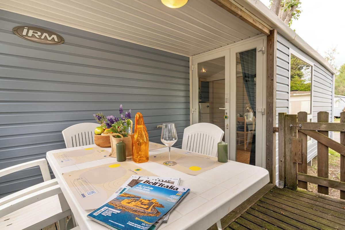 A table set with a magazine, a glass, and a candle, with a wooden fence and a door in the background.