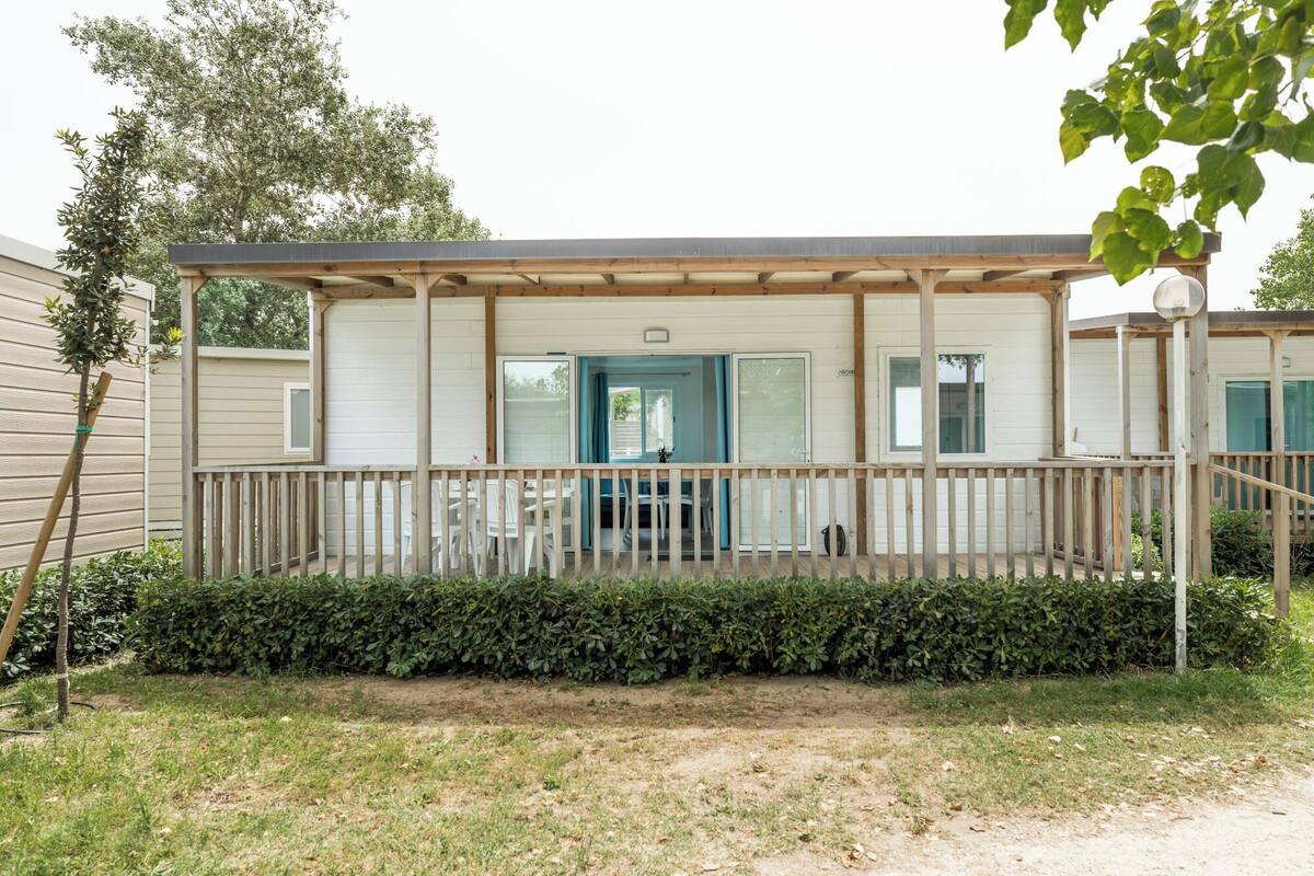 A mobile home with a covered porch, a dining area, and a small garden.
