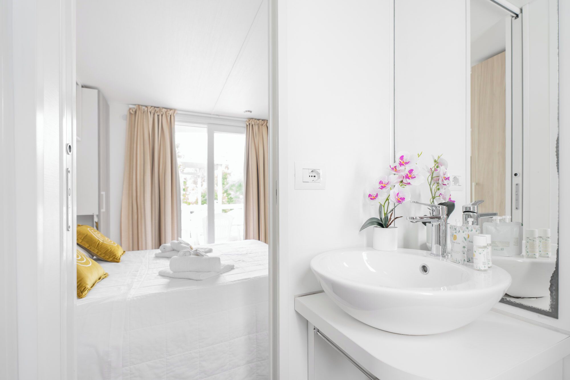 A modern hotel bathroom with a large white sink, a mirror, and a potted orchid plant.