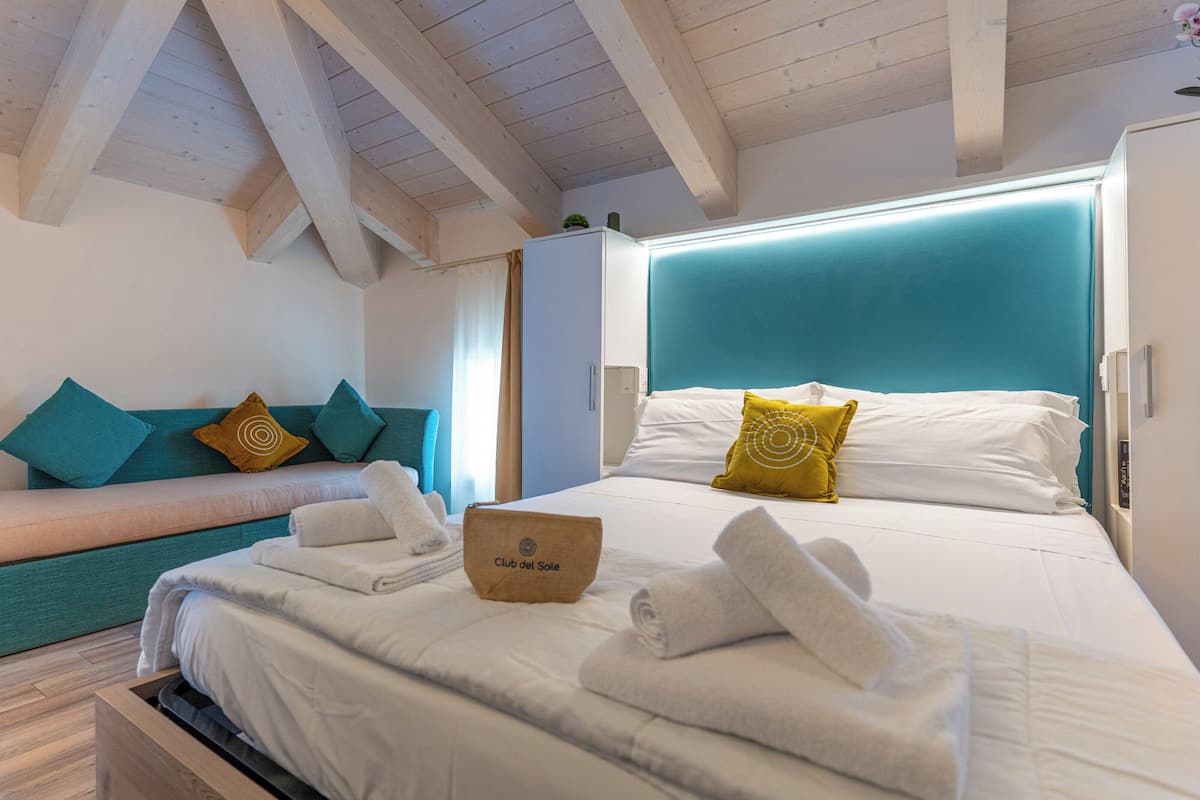 A hotel room with a bed, a sofa, and a ceiling with wooden beams.
