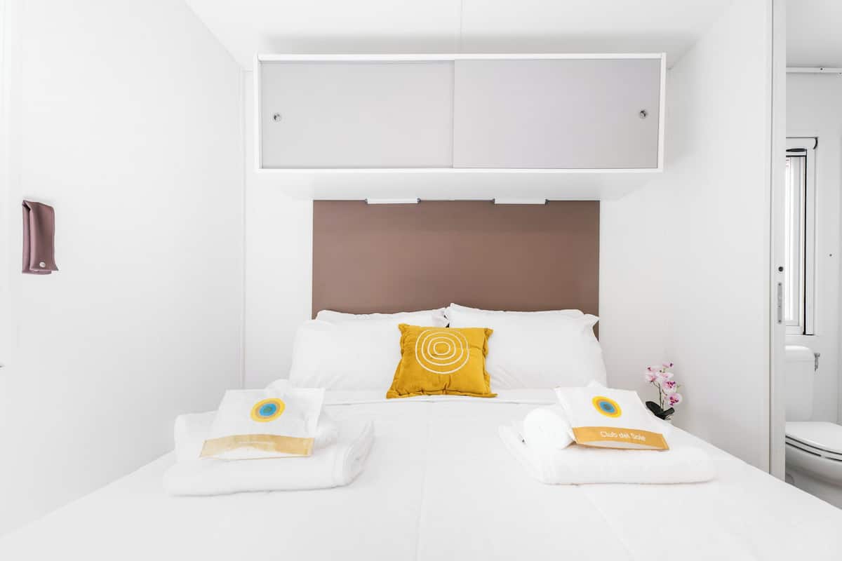 A hotel room with a bed, a headboard, a towel, and a small plant.