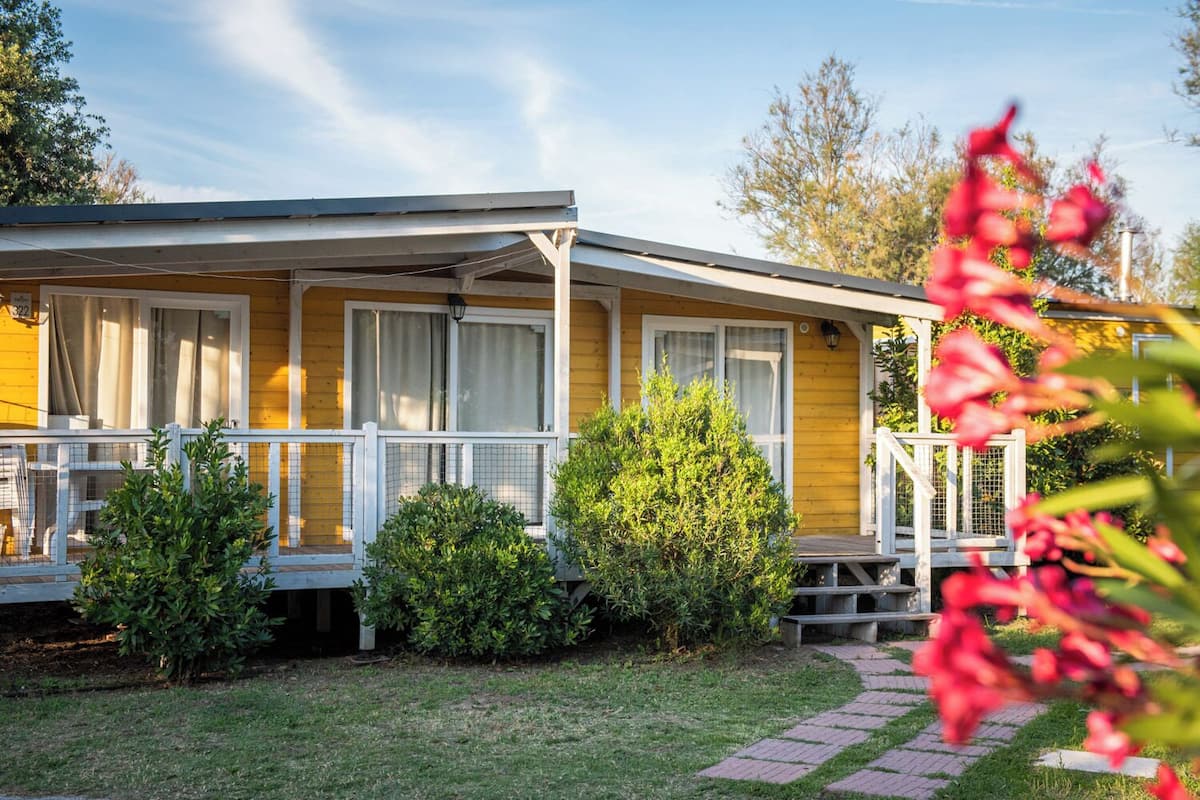 A yellow mobile home with a porch, a small garden, and a paved walkway.