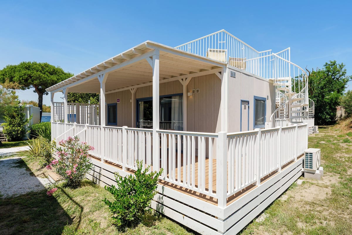 A white building with a covered porch, a staircase, and a small deck.