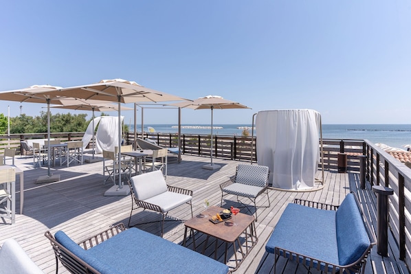 A deck with outdoor seating, umbrellas, and a view of the sea.