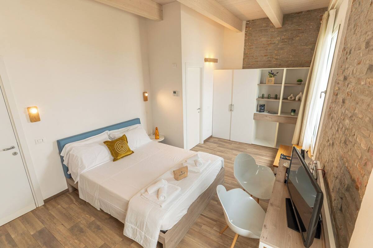 A bedroom with a bed, bedside table, chair, and a built-in TV.
