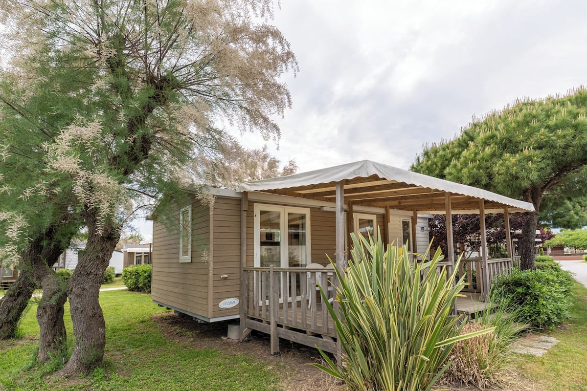 A small, single-story wooden cabin with a porch, surrounded by trees and grass.