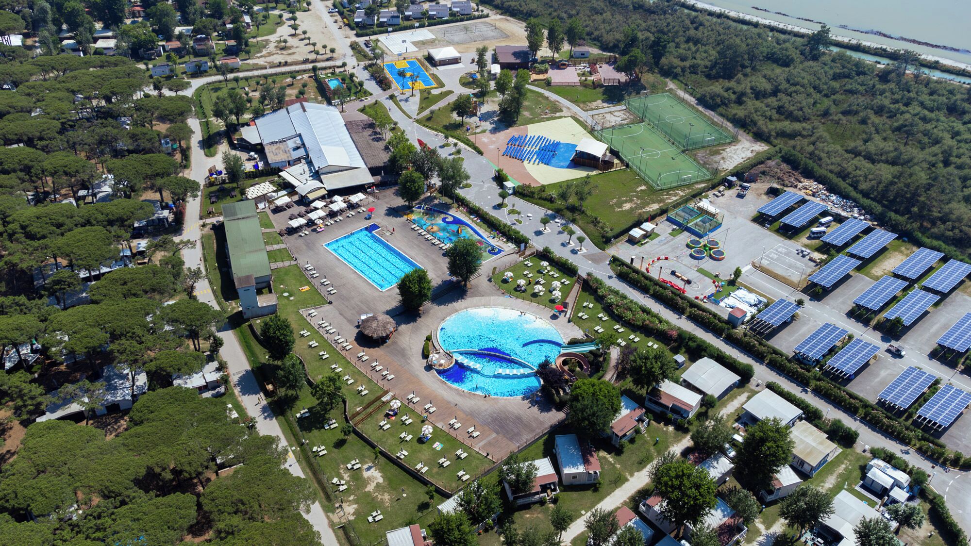 An aerial view of a resort with a swimming pool, tennis courts, and solar panels.