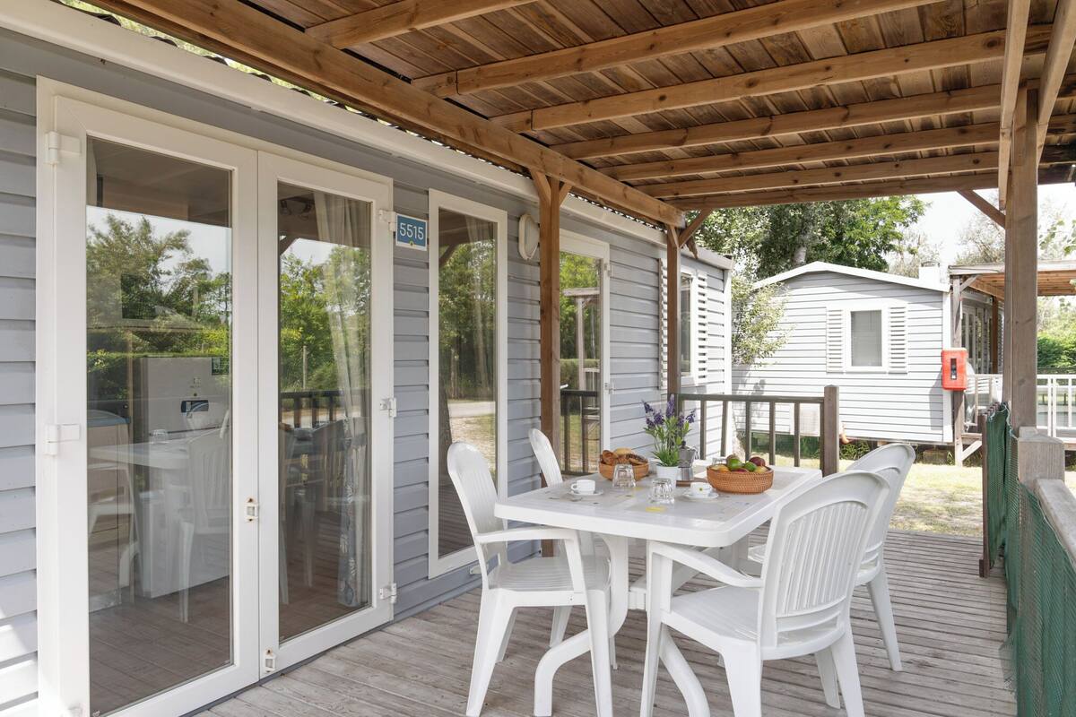 A covered patio with a table and chairs, a wooden deck, and a house in the background.