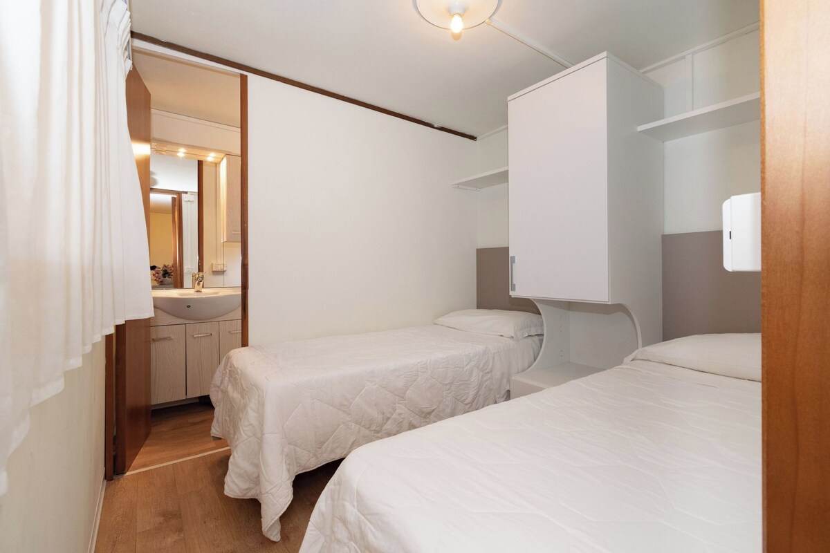 A bedroom with two single beds, a wooden floor, a white wall, and a small bathroom with a mirror and sink.