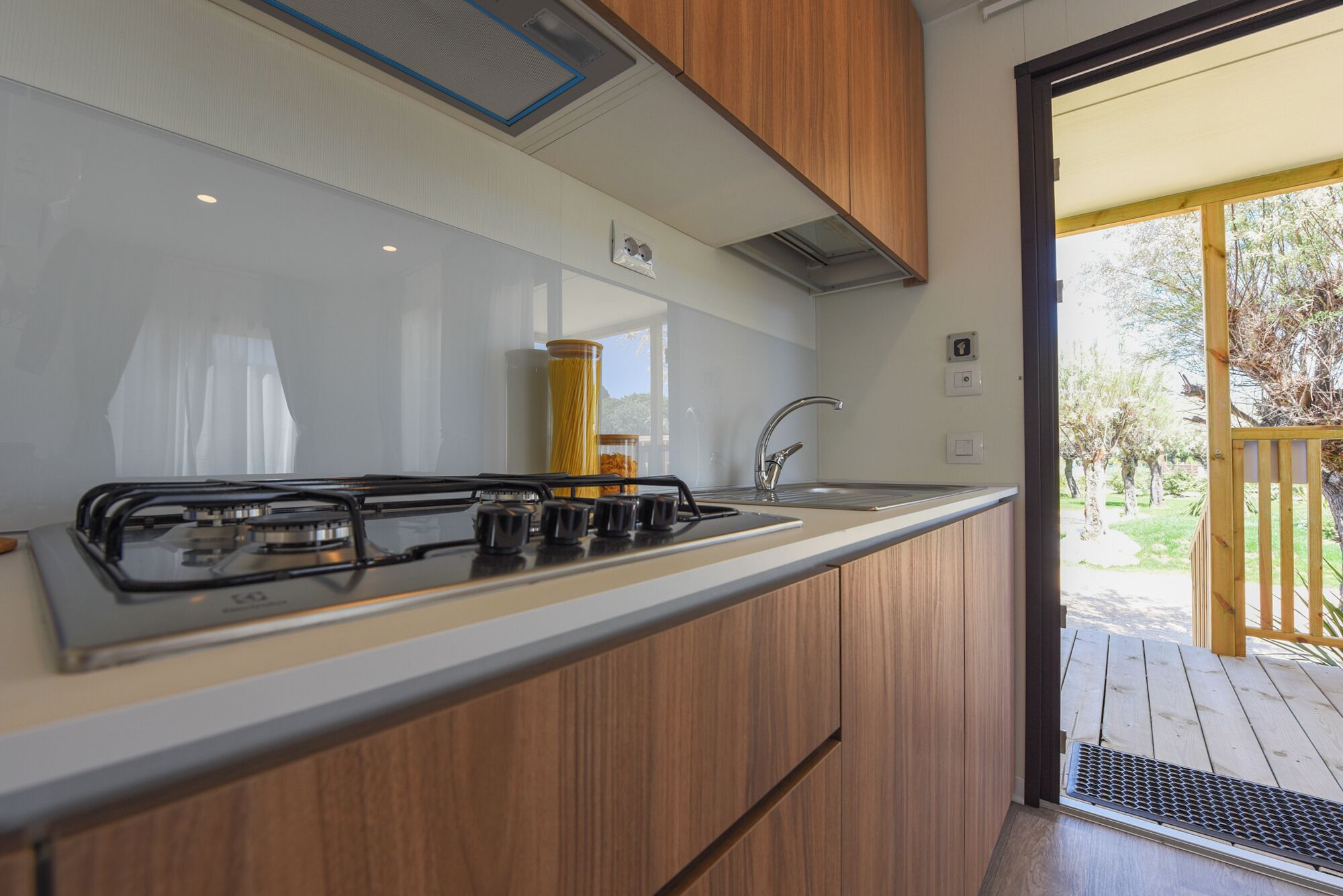 Une cuisine moderne équipée d’une cuisinière à gaz, de meubles en bois et offrant une vue sur la terrasse extérieure.