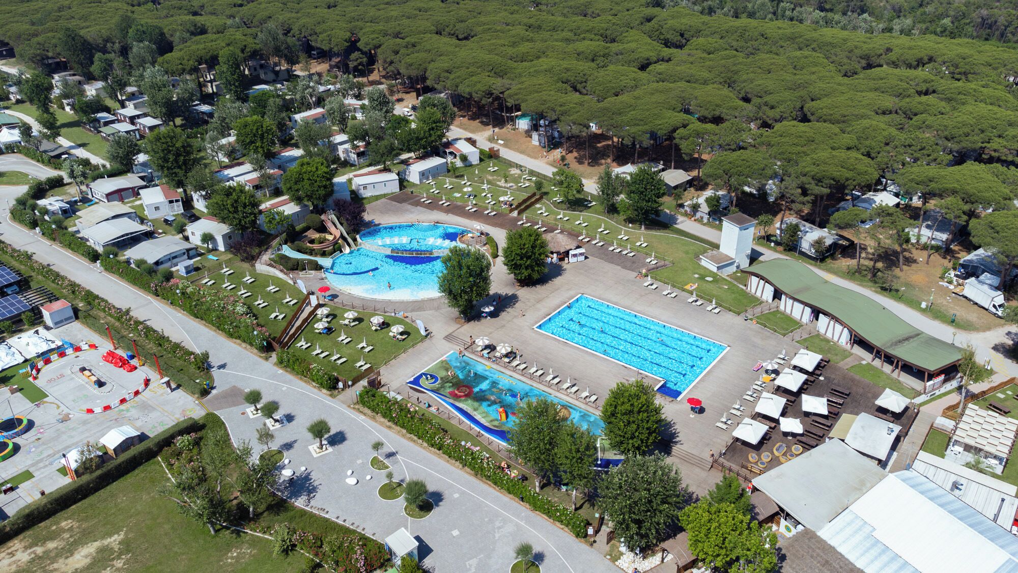 Vista aerea di un resort con diverse piscine, un ampio parcheggio e vegetazione circostante.