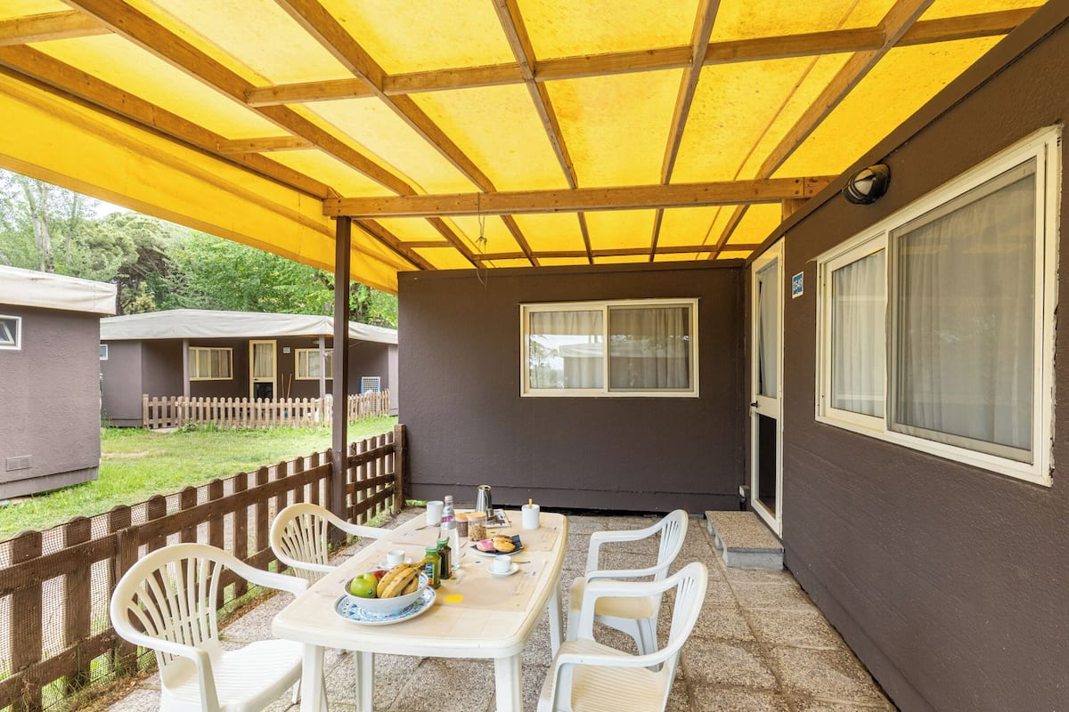 A covered patio with a table set for two, chairs, and a window with curtains.