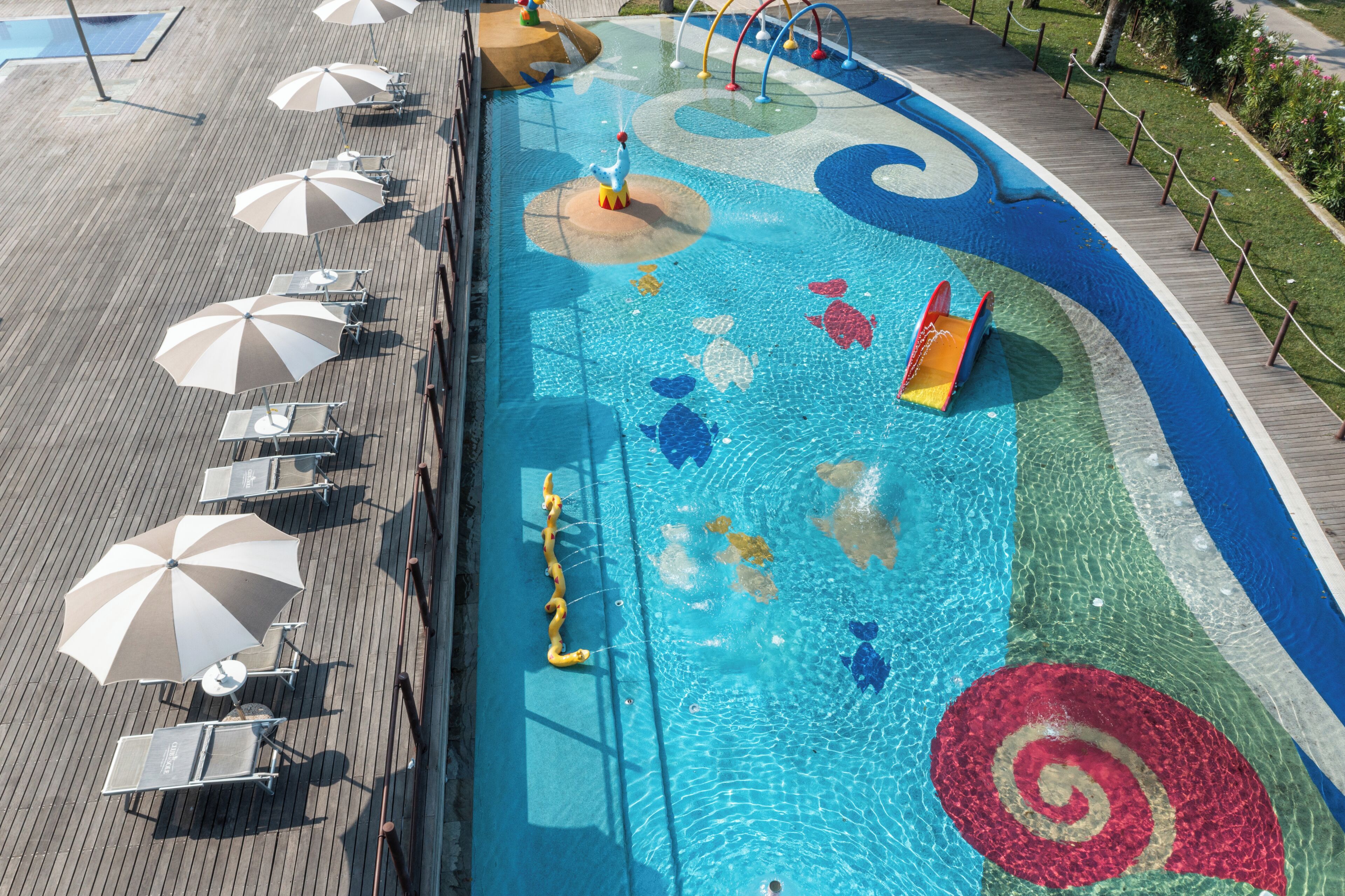 A swimming pool with colorful designs, sun umbrellas, and lounge chairs.