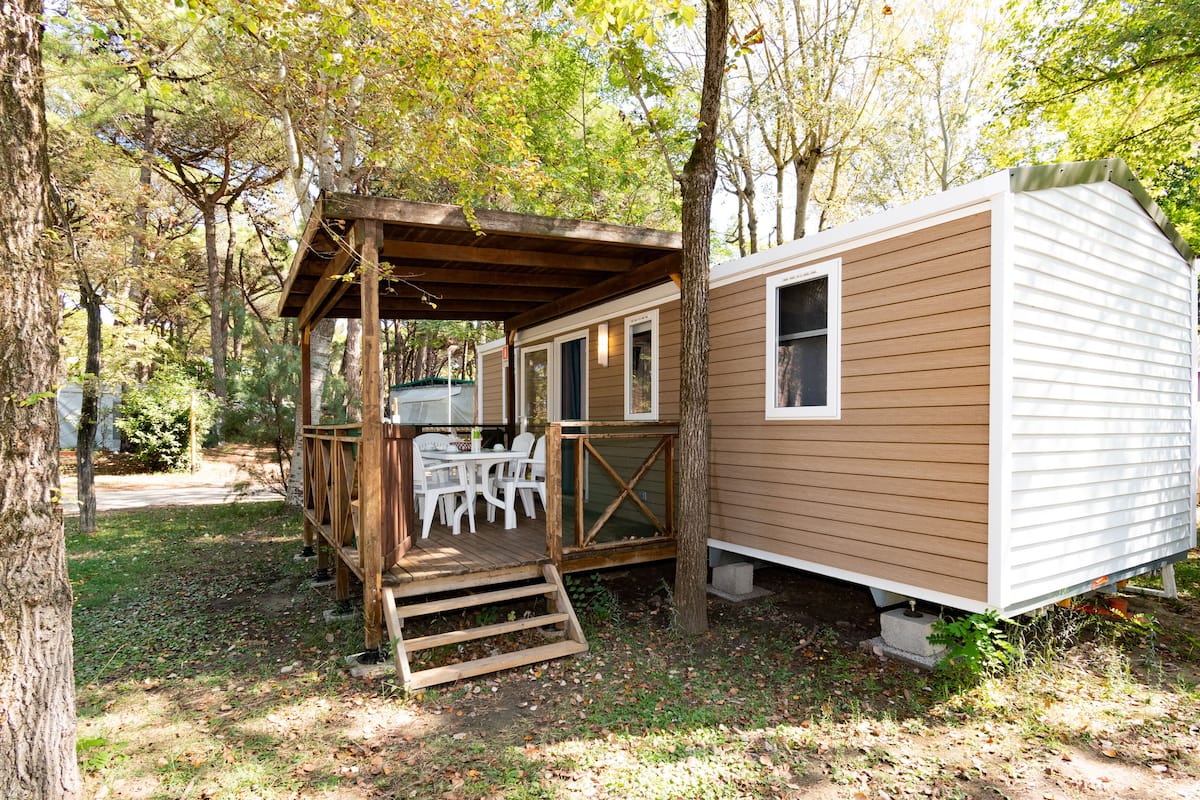 A mobile home with a wooden deck and a table with chairs.