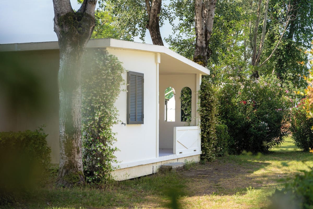 A small, single-story building with a porch, surrounded by trees and greenery.