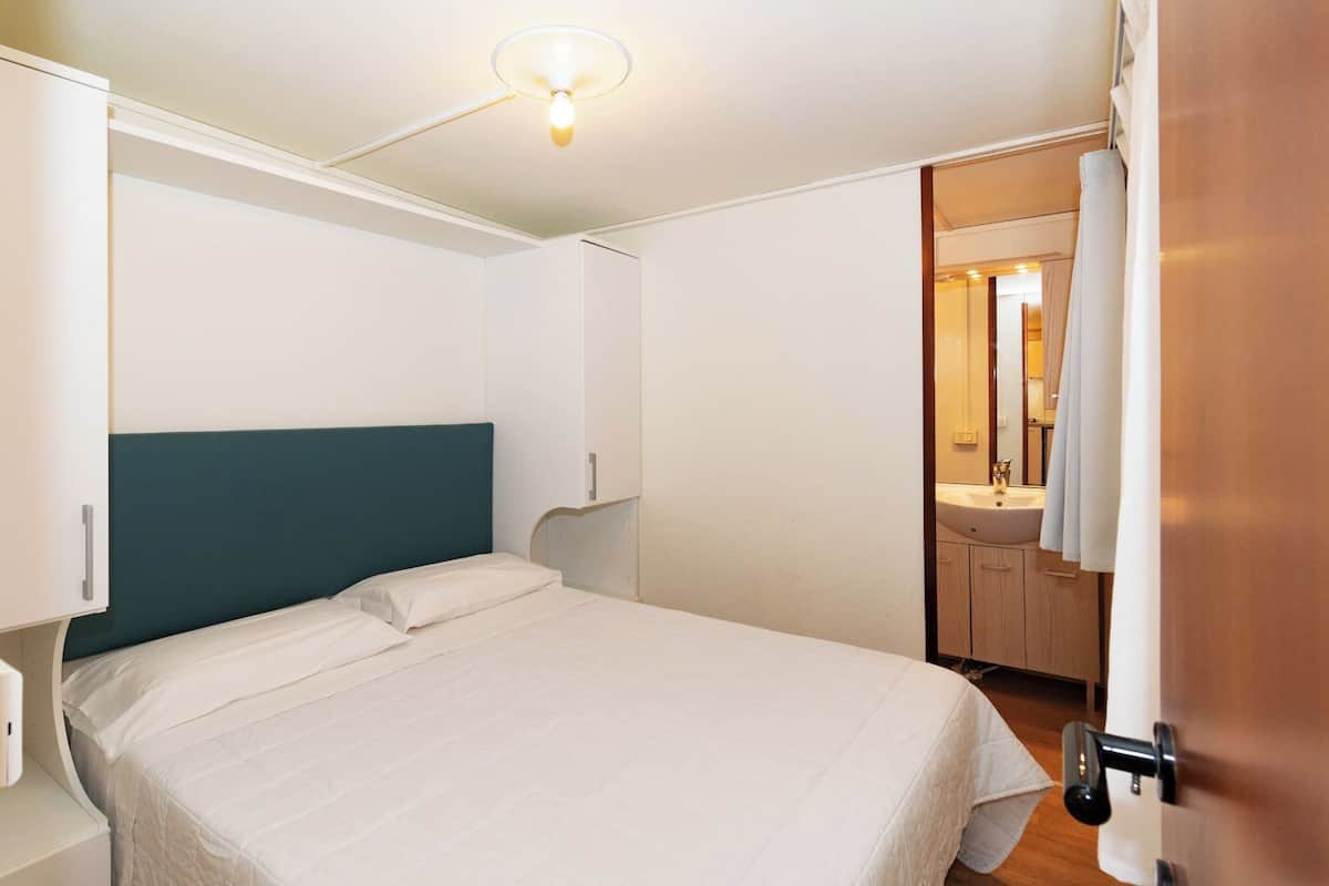 Un dormitorio con cama, mesita de noche, armario empotrado y baño visible a través de una puerta abierta.