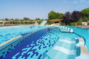 A swimming pool with a slide, surrounded by greenery and a clear sky. - Club Del Sole Spina Family Collection (Comacchio)