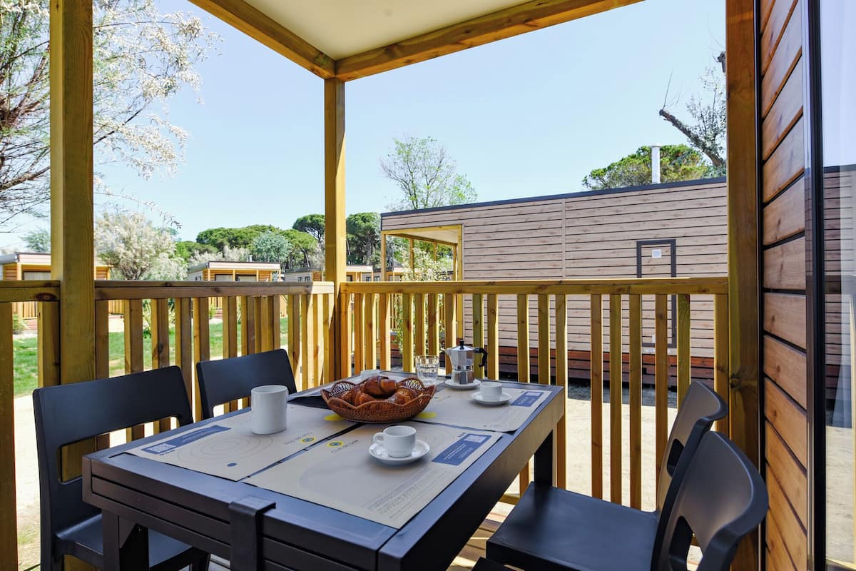A wooden deck with a table set for two, a basket of bread, and a coffee maker.