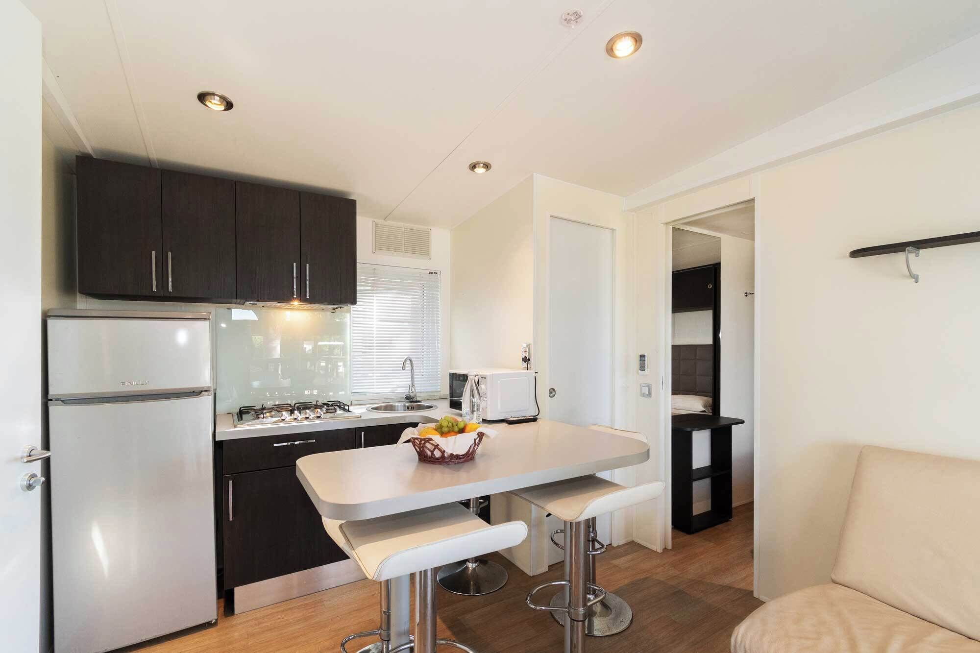 A compact kitchen with a refrigerator, stove, sink, and a small dining area with bar stools.