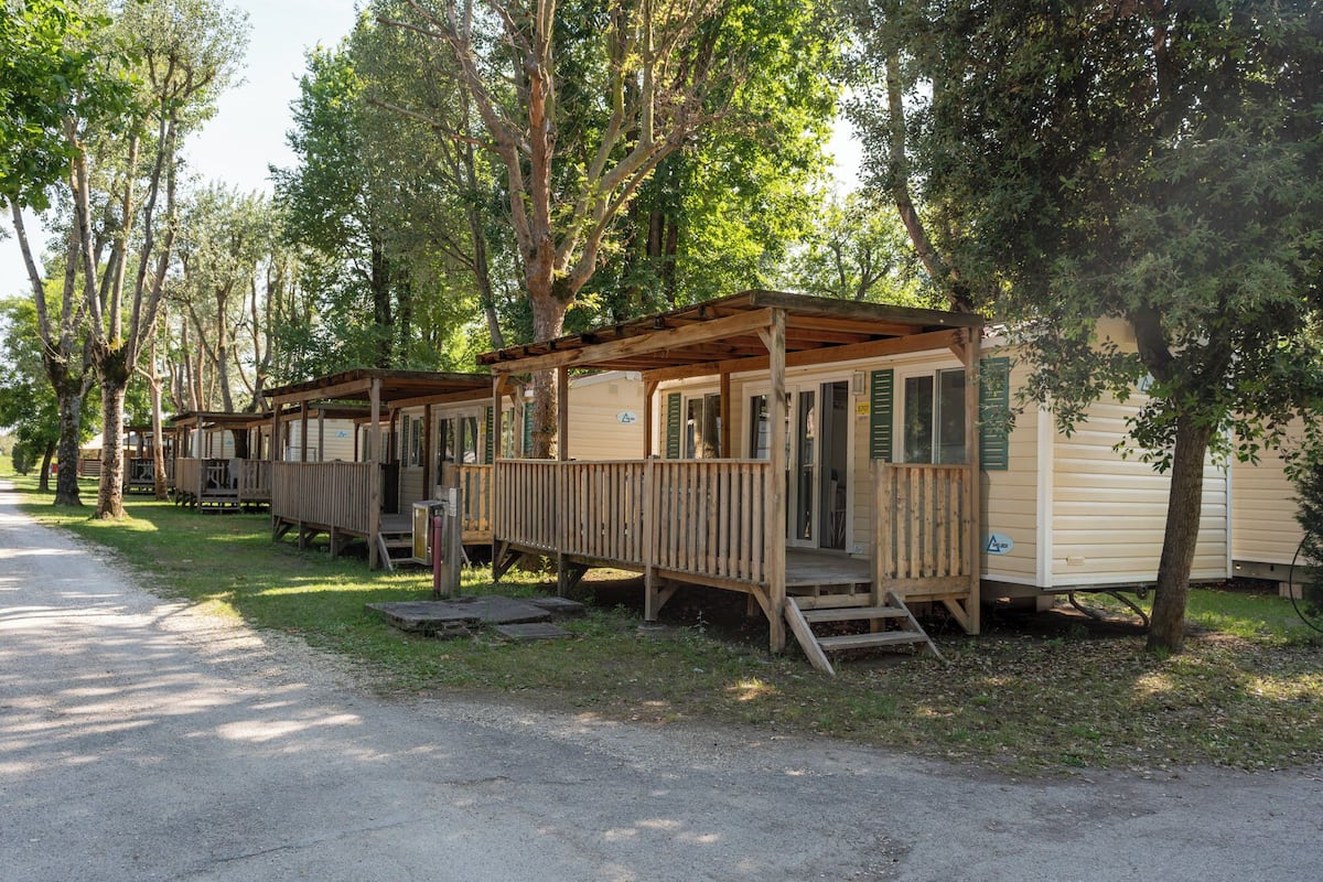 A row of mobile homes with wooden porches, surrounded by trees.