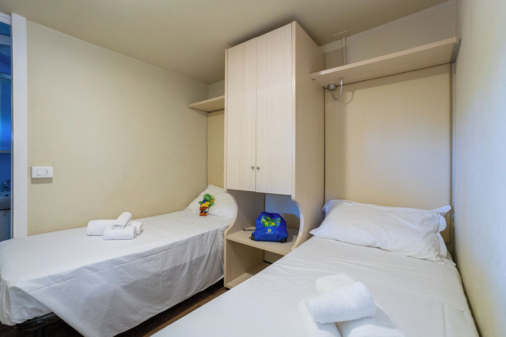 Habitación de hotel con dos camas individuales, un escritorio pequeño, un armario y zona de ducha.