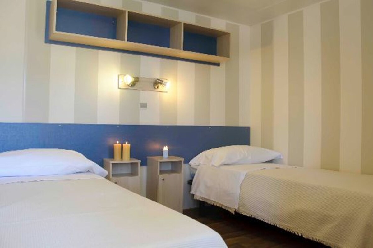 A hotel room with two single beds, a nightstand with a lamp, and a wall-mounted shelf with a light fixture.