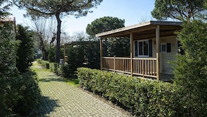 A wooden cabin with a porch, surrounded by lush greenery and trees. - Club Del Sole Marina Family Resort (Ravenna)