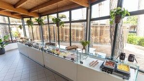 A breakfast buffet with various food options, hanging plants, and a view of the outdoors. - Club Del Sole Marina Family Resort (Ravenna)