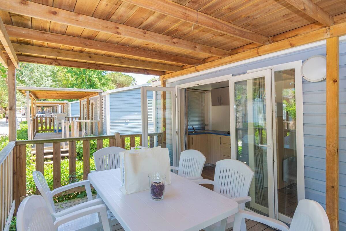A covered outdoor seating area with a table and chairs, a glass door leading to a kitchen, and a wooden deck with a railing.
