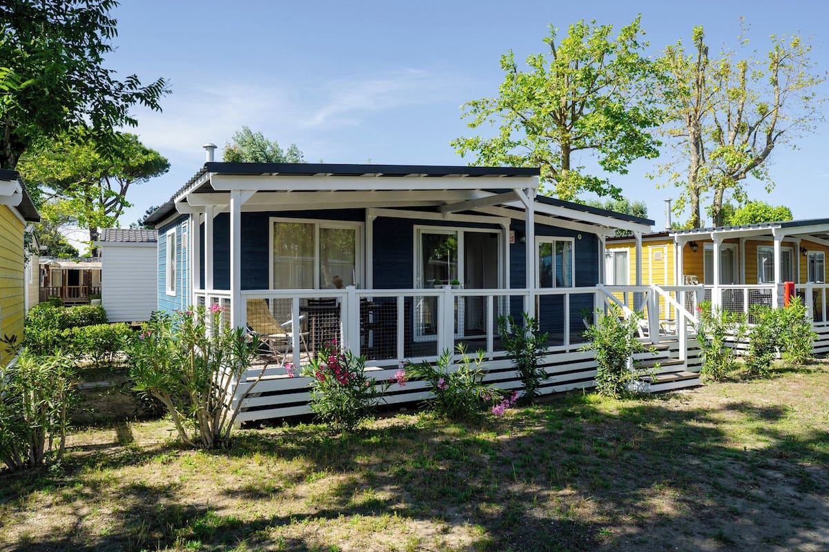 A mobile home with a porch, surrounded by greenery and other mobile homes.