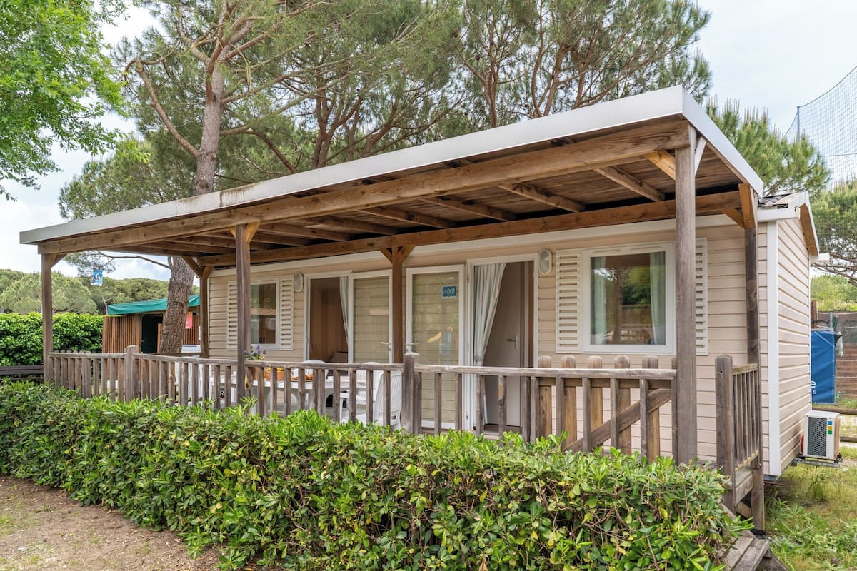 A wooden cabin with a porch, a small attached structure, and a fenced area.