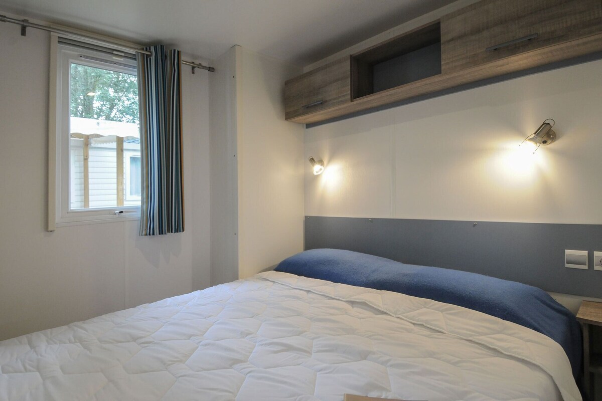 A bedroom with a bed, a window with curtains, a wall-mounted shelf, and two wall sconces.
